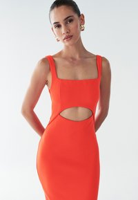 Aansluitend mouwloos jurkje in fel oranje, met een vierkante halslijn en zij uitsnijdingen. De gladde, gestructureerde stof benadrukt de vorm.