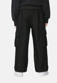 Czarne dżinsowe spodnie cargo o luźnym kroju, elastycznym pasie, dwóch bocznych kieszeniach i widocznych detalach szwów. Noszone z białymi skarpetkami.