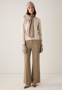 Pull en maille beige avec accents floraux, écharpe assortie, pantalons larges marron, gants beige, et talons pointus marron.