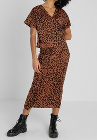 Hnědý leopardí vzorovaný top a odpovídající sukně; krátké rukávy; V-červěný výstřih; měkká látka; stylizováno s černými bojovými botami a kruhovými náušnicemi.