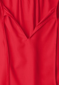 Gros plan d'un tissu rouge avec un col en V, coutures visibles et détails des coutures.