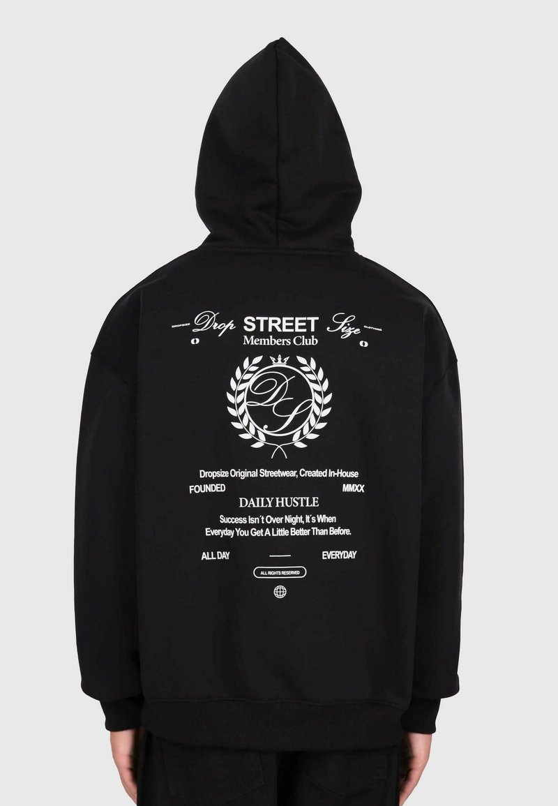 Czarna bluza z kapturem z białym napisem "Drop Street Members Club", grafiką wieńca laurowego i motywującym cytatem z tyłu, noszona przez osobę stojącą tyłem.