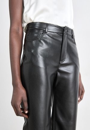 Des pantalons taille haute en simili cuir noir présentent une texture lisse, des poches avant et une fermeture éclair avec un seul bouton.