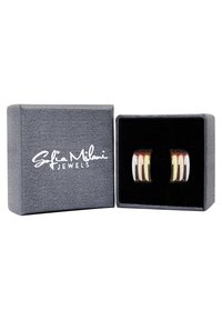 Silvriga och guldfärgade örhängen med en slät, texturerad yta i en visningslåda med en matt grå utsida och svart sammet inuti.