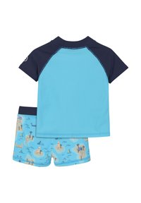 Tvådelad badset bestående av en ljusblå topp med kort ärm och marinblå detaljer samt mönstrade baddräktsshortsen som visar strandscener och båtar.