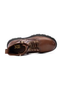 Bota de tobillo de cuero marrón con suela de goma negra, que cuenta con ojales y cordones en tono dorado, además de una lengüeta para facilitar su uso. Marca interior visible.