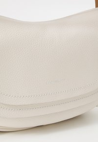 Borsa a tracolla in pelle beige con texture a ciottoli, design curvo, cuciture argentate e logo del marchio in rilievo sulla parte anteriore.