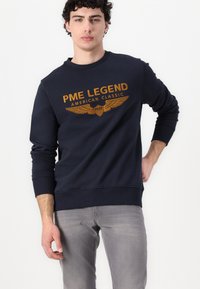 Marine pullovertrui met geribbelde manchetten en zoom. Voorzien van een voorprint in oranje met een adelaarsontwerp en de tekst "PME Legend American Classic".