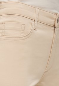Pantalones de mezclilla beige con un bolsillo lateral, textura suave y costuras contrastantes a lo largo de las costuras y la cinturilla.