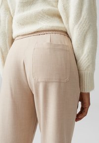 Lichtbeige op maat gemaakte broeken met een zachte textuur, voorzien van een enkele achterzak en een elastische tailleband, gecombineerd met een crèmekleurige gebreide trui.