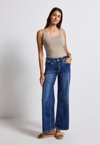 Jeans anchos azules con una cintura a media altura, hechos de mezclilla. Combinados con una blusa sin mangas de color beige claro, con escote redondeado.