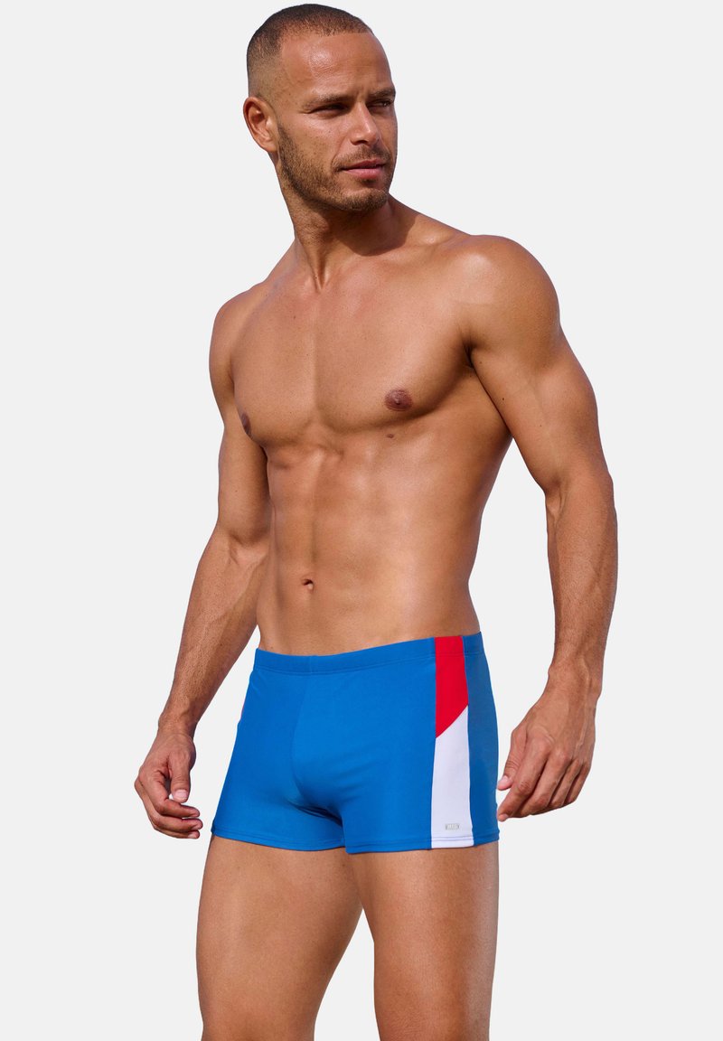 Blauwe zwembroek met rode en witte accenten aan de zijkant. Gemaakt van rekbaar materiaal met een aansluitend ontwerp voor comfort en beweging.