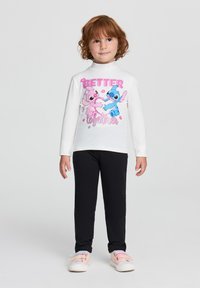 Camicia bianca a maniche lunghe con una grafica colorata che presenta personaggi dei cartoni animati, abbinata a leggings neri e scarpe dai colori pastello.