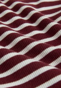 Materiał w burgundowo-białe paski o prążkowanej fakturze, z na przemian gładkimi i wypukłymi paskami tworzącymi falisty wzór.