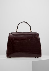 Burgundy lackläderhandväska med texturerat krokodilsmönster, strukturerad form, kort handtag och detaljer i guldton.