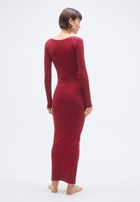 Bordové priliehavé šaty s dlhým rukávom a s výstrihom na chrbte, vyrobené z hladkej pružnej tkaniny, s dĺžkou do polovice lýtok, s minimalistickým dizajnom.