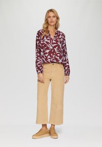 Bordeaux bloemenblouse met lange mouwen, beige wijde broek en tan sneakers met een gestructureerde zool. Eenvoudige halslijn en relaxed fit.