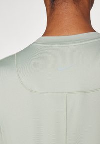 Camiseta deportiva Nike de color verde claro con textura suave, cuello redondeado y un diseño minimalista que incluye un pequeño logo pálido en la parte posterior.