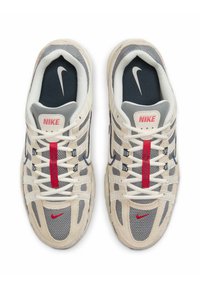 Nike sneakers featuring a beige suede and gray mesh upper, white laces, red accents, and a navy interior with branding details.