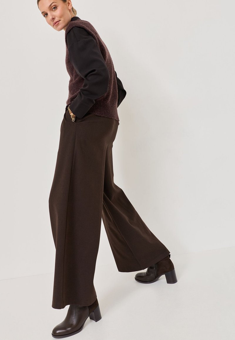 Un pantalon large marron associé à un pull texturé sombre et des bottes à talons épais. La tenue présente des matériaux et des couleurs contrastants.