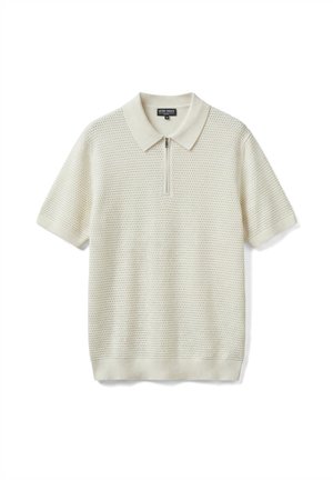 Polo de punto color crema de manga corta con patrón texturizado, cuello y cierre frontal con cremallera, colocado sobre un fondo blanco.