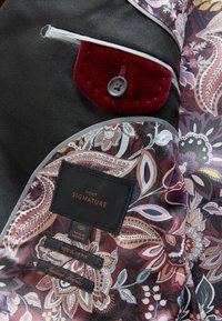 Fekete anyag virágmintás béléssel. Jellemzője egy bordó bársonyzseb gombbal, méret- és illeszkedési címkék, valamint kontrasztos díszítés.