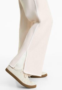Bløde lyserøde brede bukser med hvide sidelister og splitkant. Sættes sammen med lysebeige sneakers og hvide sokker.