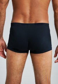 Boxer in nero realizzati in tessuto liscio e elastico. Presentano un morbido elastico in vita e un design aderente che si adatta al corpo.