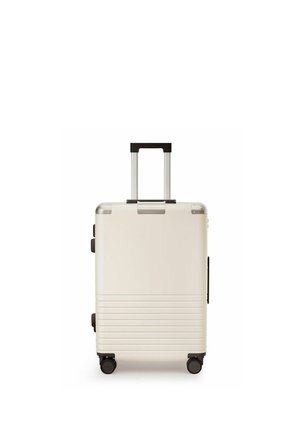 Cremefarbener Hartschalenkoffer mit vier schwarzen Spinner-Rollen und einem nach oben ausgezogenen schwarzen Teleskopgriff.