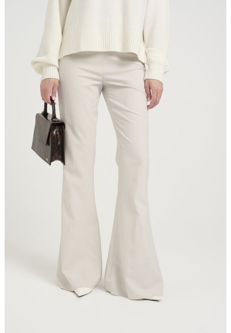 Pantalon évasé beige clair avec une texture lisse et une coupe sur mesure. Porté avec un pull en maille crème et un petit sac à main foncé.