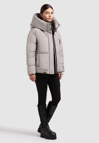 Grijze gevoerde jas met een grote capuchon, ritssluiting, horizontaal gestikt ontwerp en zijzakken. Gecombineerd met zwarte leggings en kniehoogtelaarzen.