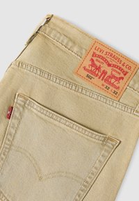Μπεζ τζιν Levi's 502 που εμφανίζουν την πίσω τσέπη, την κόκκινη ταμπέλα Levi's και το δερμάτινο ετικέτα με το μέγεθος W32 L32.
