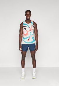 Mænds atletiske tøj bestående af en farverig tanktop med abstrakt mønster i let stof og navy shorts. Hvide sneakers med detaljer fuldender looket.