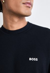 Marinblå sweatshirt med ribbad textur, försedd med en liten vit "BOSS"-logotyp på vänster sida av bröstet. Klassisk design med rund halsringning.