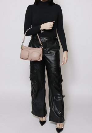 Person wearing black long-sleeve top and black leather cargo pants, holding a beige handbag with two front pockets.