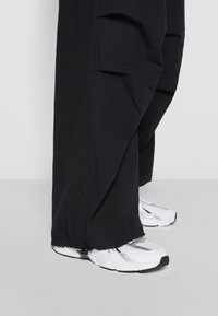 Svarta vida cargobyxor i texturerad tyg, med stora fickor och elastiska muddarna, kombinerat med vita och silverfärgade sportskor.