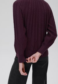 Lila gestrickter Pullover mit einem strukturierten Muster, ausgestattet mit gerippten Bündchen und Saum. Der Rücken zeigt starke vertikale Linien und gedrehte Motive.