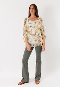 Blusa leggera con stampa floreale in morbidi pastelli, con una vestibilità ampia e maniche a pipistrello. Abbinata a pantaloni a campana verde oliva attillati e sandali marroni.