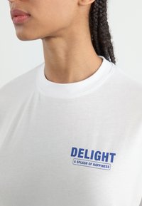 Hvid bomulds t-shirt har blå tekst "DELIGHT" og undertekst "A SPLASH OF HAPPINESS" foran, rund halsudskæring og korte ærmer.