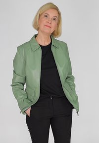 Lichtgroene leren jas met ritssluiting, kraagontwerp en zijzakken. Draag het over een zwarte top en combineer het met zwarte broek.
