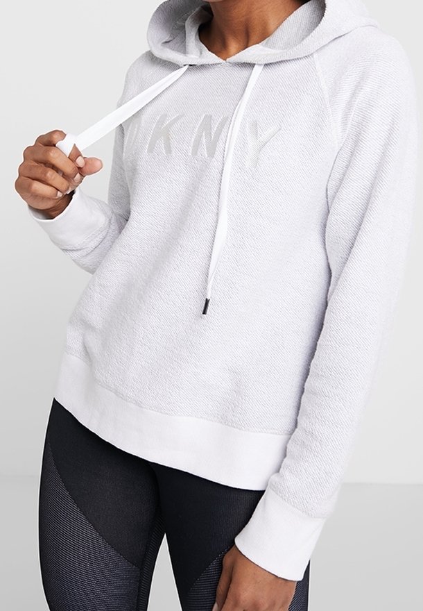 Ljust grå hoodie i texturerad tyg, vita dragsko, och en diskret präglad "DKNY"-logotyp på framsidan. Vita manschetter.