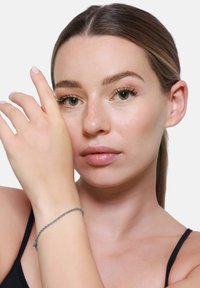 Silberfarbenes geflochtenes Armband, das an einem Handgelenk getragen wird, und die komplexe Webart sowie der zarte Verschluss zeigen kann, vor einem neutralen Hintergrund.