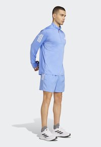 Light blue athletic long-sleeve polo and shorts, featuring three white stripes on sleeves, paired with white sneakers and gray socks.