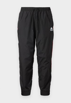 Černé teplákové kalhoty Kappa s elastickým pasem a manžetami, šňůrkou vpředu a bílým logem na horní části stehna s červenými bočními pruhy.