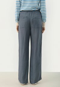Grijze, wijde broek met een elastische tailleband en twee achterzakken. De stof lijkt lichtgewicht met een gladde textuur.