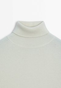Pull à col roulé côtelé de couleur crème avec un col plié et un tissu en maille lisse, vu du buste sur un fond blanc.