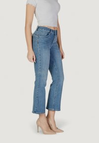 Jeans de mezclilla azul claro con corte recto, dobladillo deshilachado y diseño de cinco bolsillos. Combinados con zapatos de tacón nude y una blusa blanca ajustada.