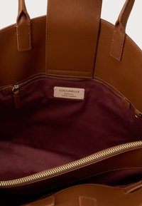 Καφέ δερμάτινη τσάντα ώμου με εσωτερικό από μπορντό ύφασμα, με χρυστό φερμουάρ και μικρή ετικέτα που γράφει "Coccinelle Authentic Italian Leather".