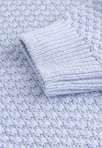 Gros plan d'une manche de pull tricoté bleu clair montrant un poignet côtelé et un motif de tricot texturé sur un tissu doux.