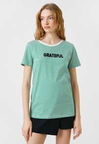 Grøn- og hvidstribet t-shirt med korte ærmer, rund halsudskæring og sort "GRATEFUL" tekst foran. Blødt stof, afslappet pasform.